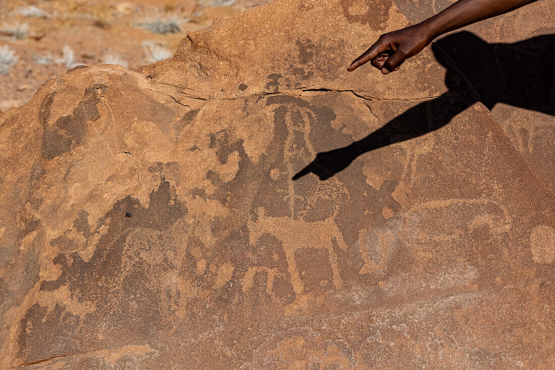 Die Hand und der Schatten eines Mannes zeigen auf eine alte Felsgravur, Twyfelfontein, Damaraland; Kunene Region, Namibia