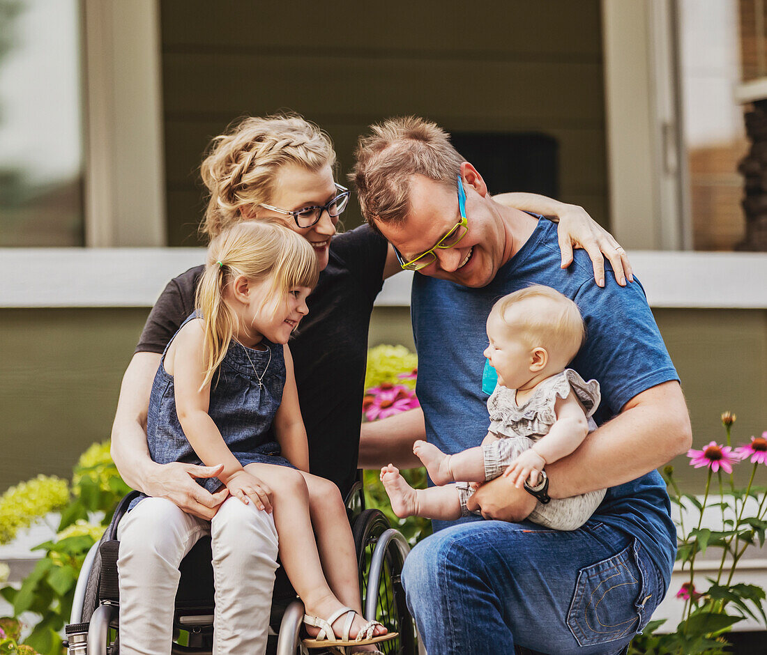 Eine junge Familie posiert für ein Familienporträt in ihrem Vorgarten, und die Mutter ist querschnittsgelähmt und sitzt im Rollstuhl; Edmonton, Alberta, Kanada