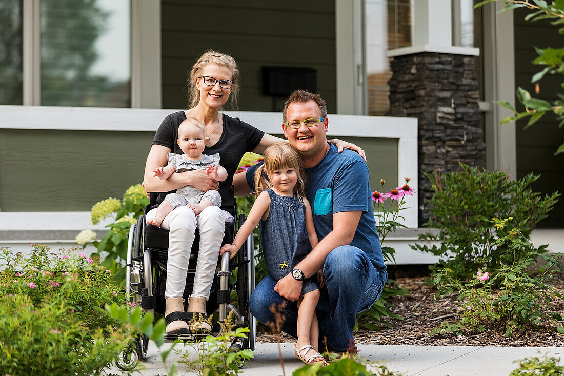 Eine junge Familie posiert für ein Familienporträt in ihrem Vorgarten, die Mutter ist querschnittsgelähmt und sitzt im Rollstuhl; Edmonton, Alberta, Kanada