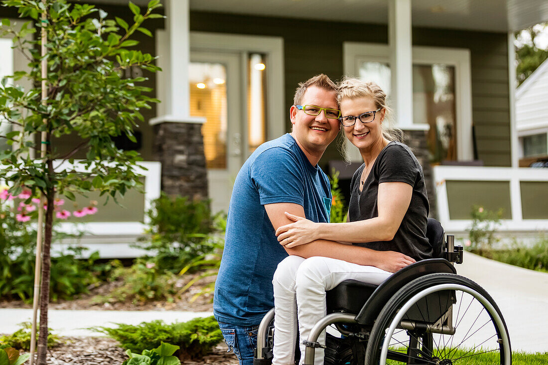 A husband and his paraplegic wife posing for a family photo in their front yard on a warm fall day: Edmonton, Alberta, Canada