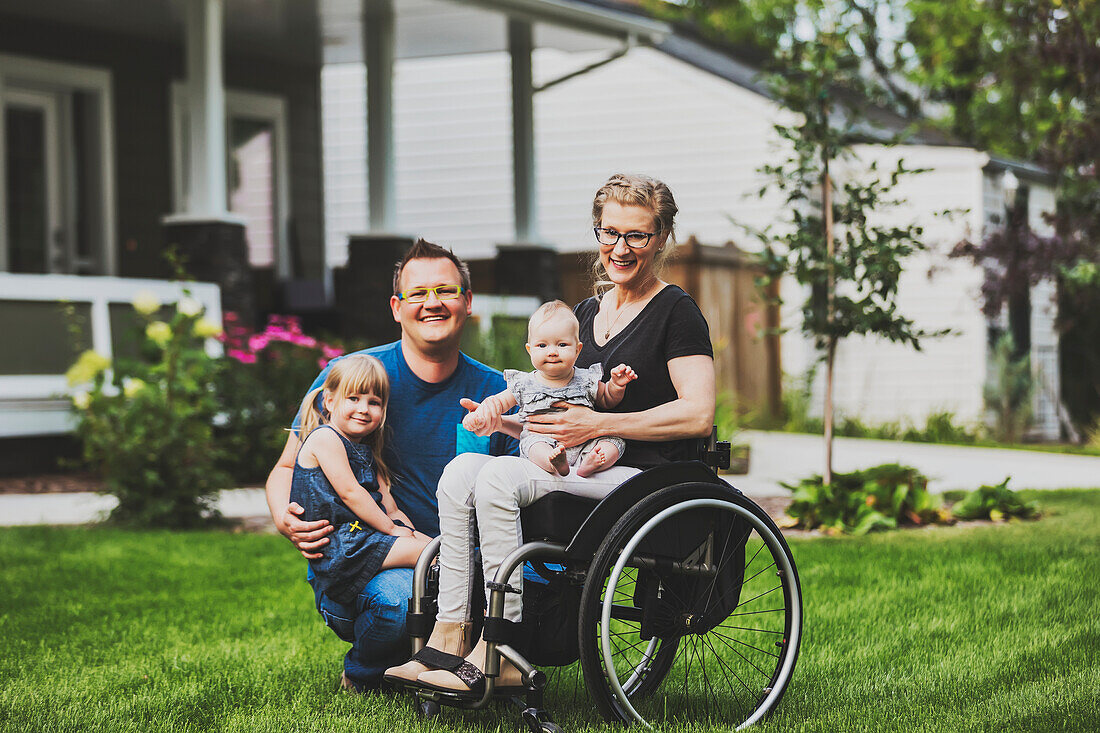 A young family posing for a family portrait outdoors in their front yard and the mother is a paraplegic in a wheelchair; Edmonton, Alberta, Canada