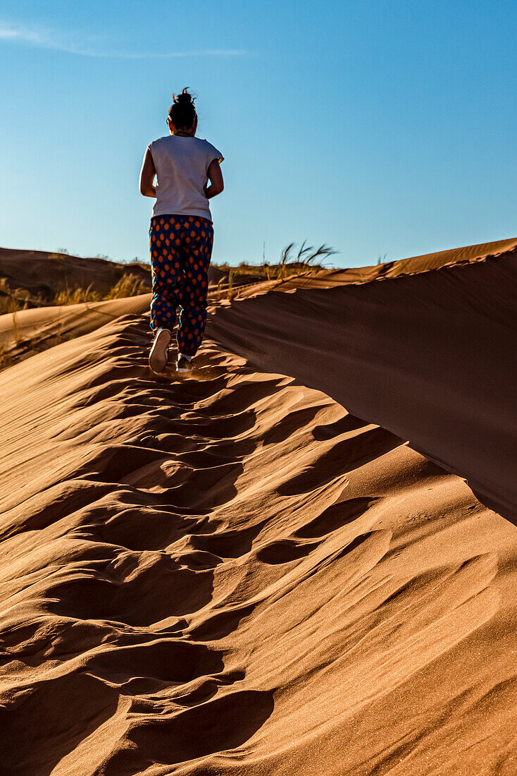 Female tourist walks up a sand dune, Elim dune, Namib Desert; Sesriem, Namibia