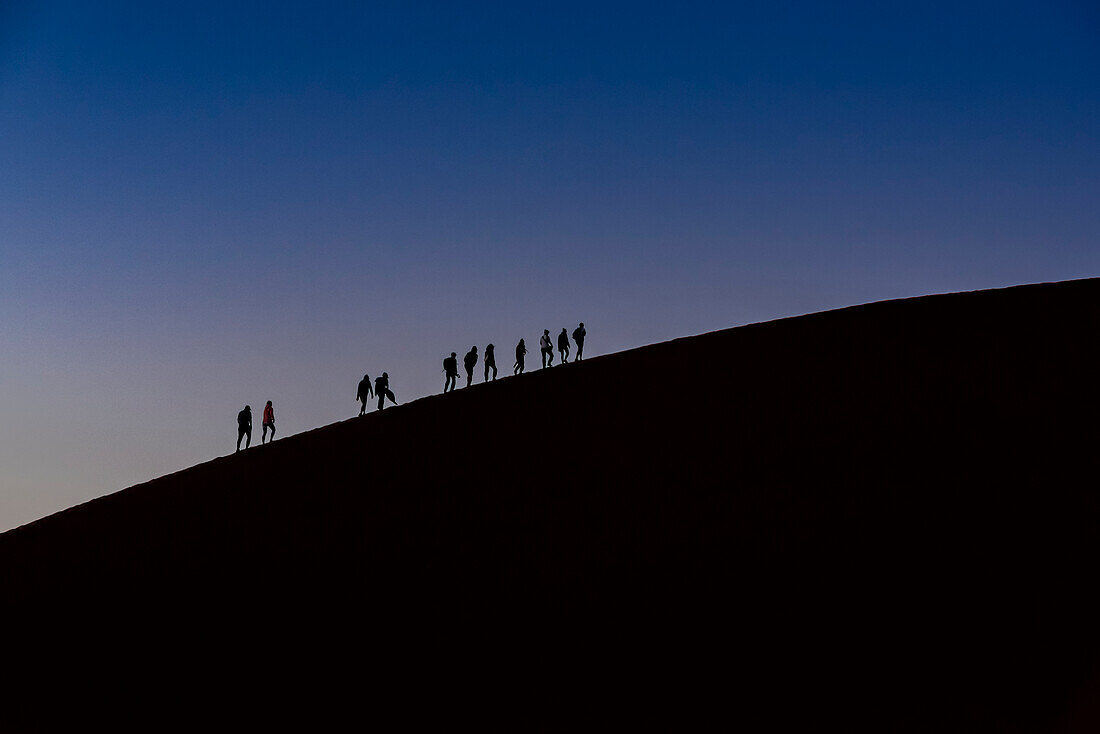 Silhouette von Touristen beim Besteigen der Düne 45 in der Abenddämmerung, Sossusvlei, Namib-Wüste; Namibia