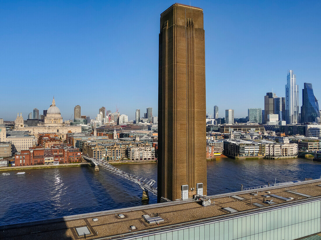 Schornstein des Kunstmuseums Tate Modern und die Millennium Bridge, die die Themse überquert, mit einer Stadtansicht von London; London, England