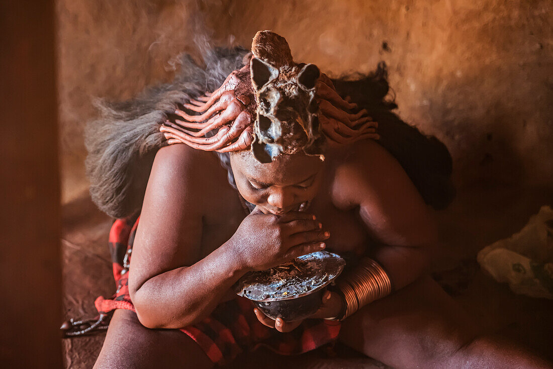 Himba-Frau bereitet Weihrauch vor, um ihr Haar mit dem Rauch zu waschen, Himba-Dorf; Kamanjab, Namibia
