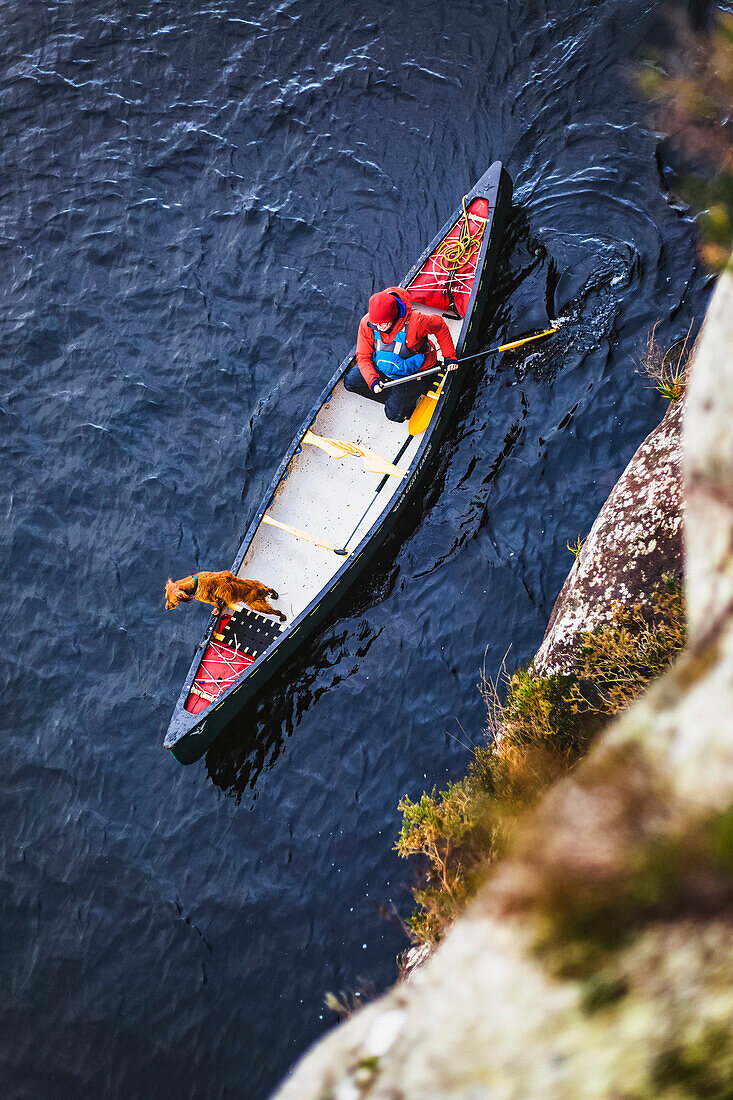 Blick von oben auf eine Frau und einen Hund beim Paddeln auf einem See in Irland im Winter, Killarney National Park; County Kerry, Irland