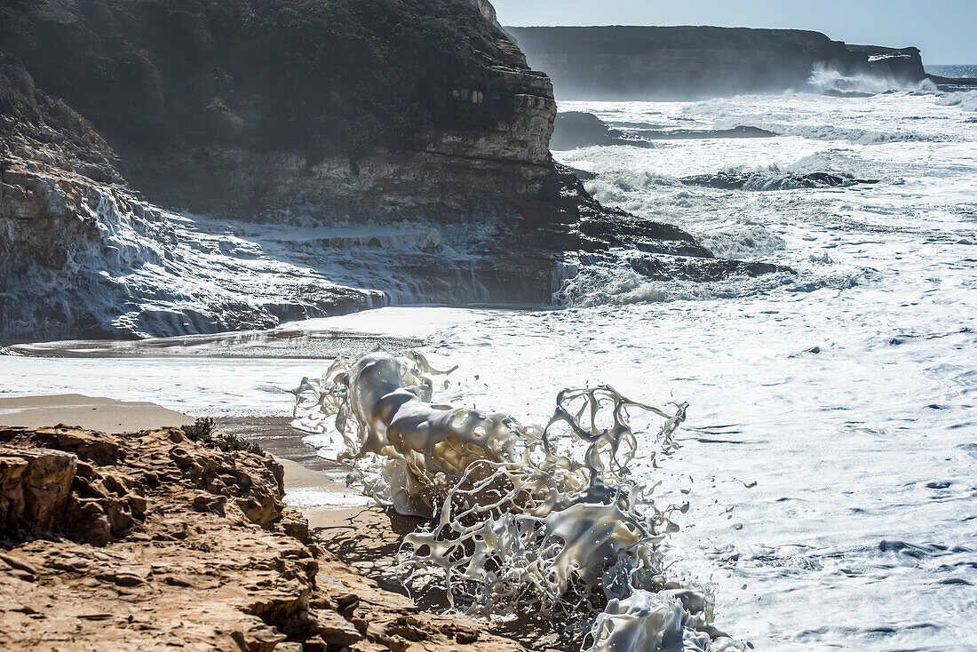 Beach foam created by waves crashing onto a beach at Wilder Ranch State Park; California, United States of America