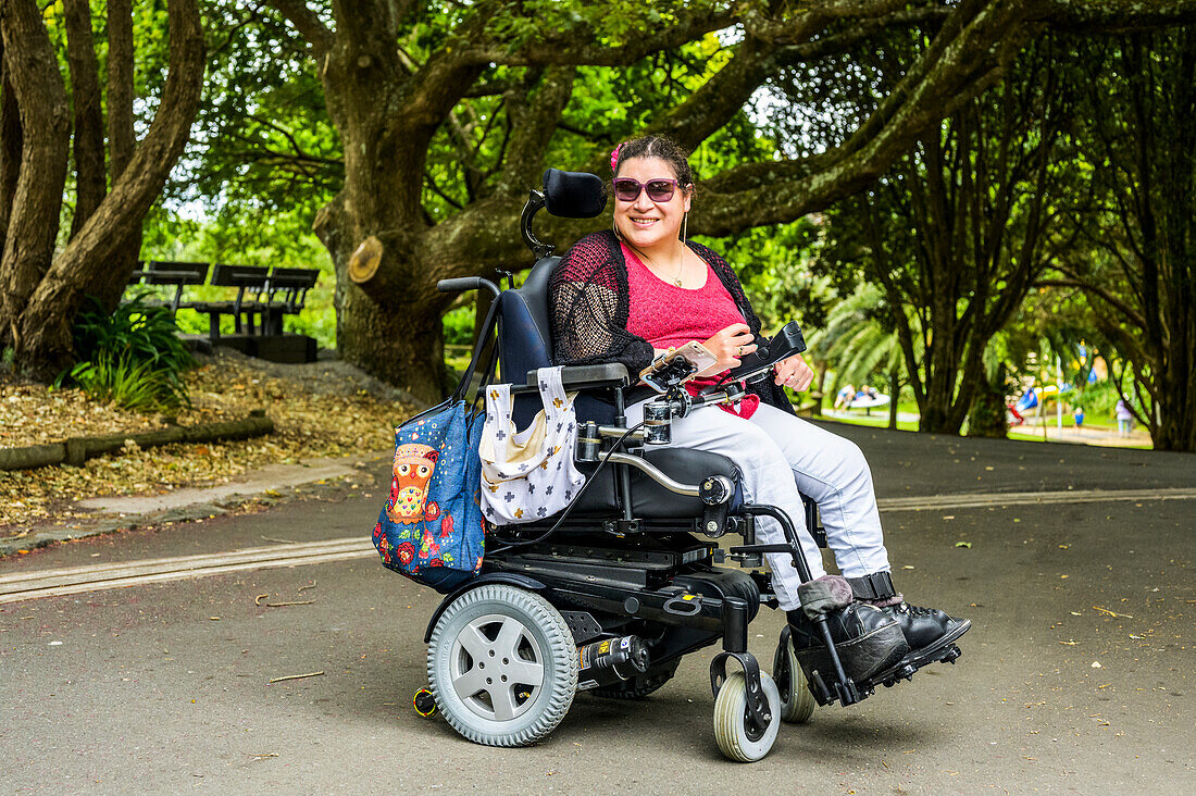 Maori-Frau mit Cerebralparese in einem Rollstuhl in einer Parkanlage; Wellington, Neuseeland