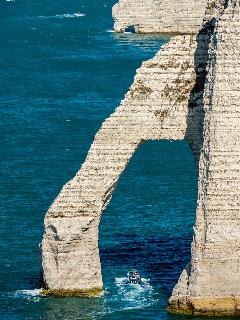 Natural arch in the chalk cliffs with teal coloured water along the coast, Etretat Chalk Complex; Etretat, Normandy, France