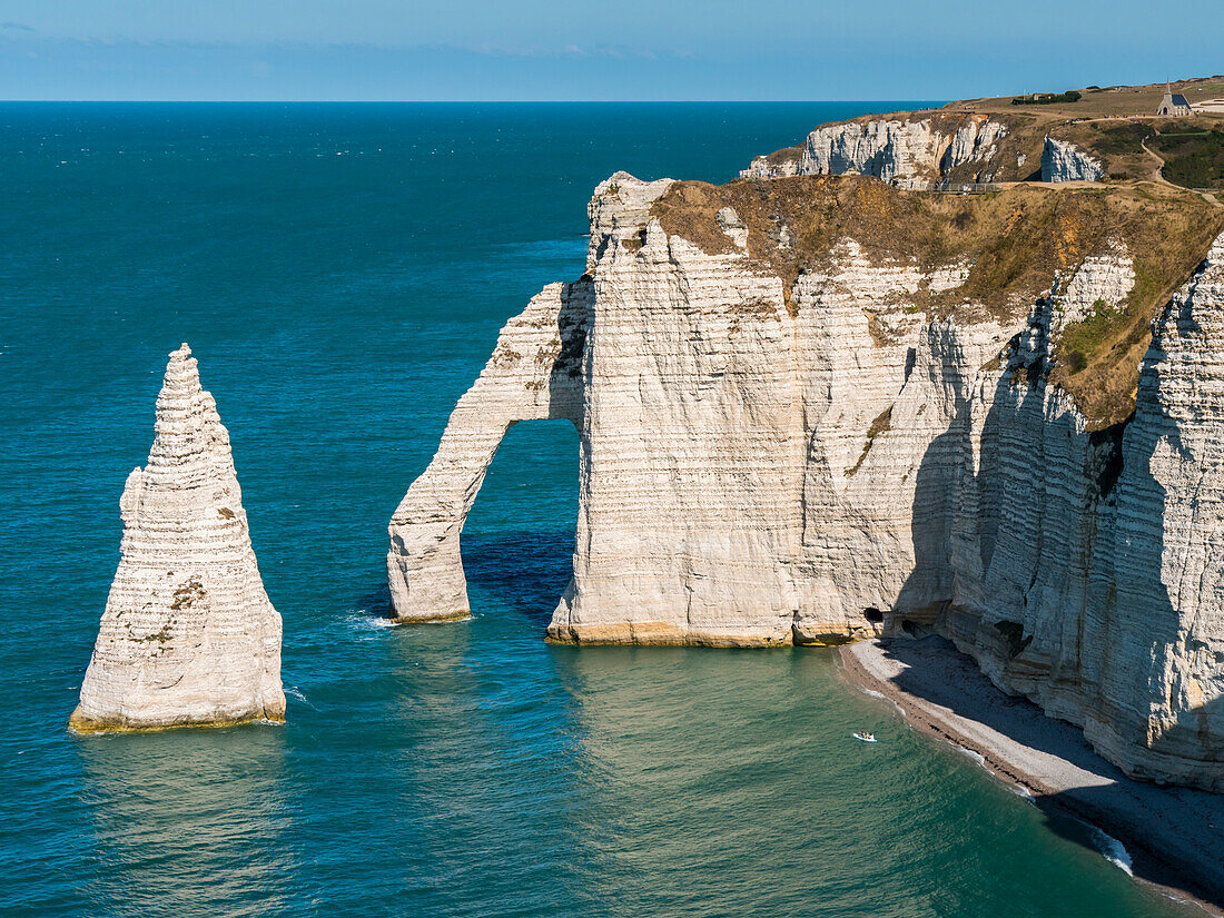 Natural arch in the chalk cliffs with teal coloured water along the coast, Etretat Chalk Complex; Etretat, Normandy, France