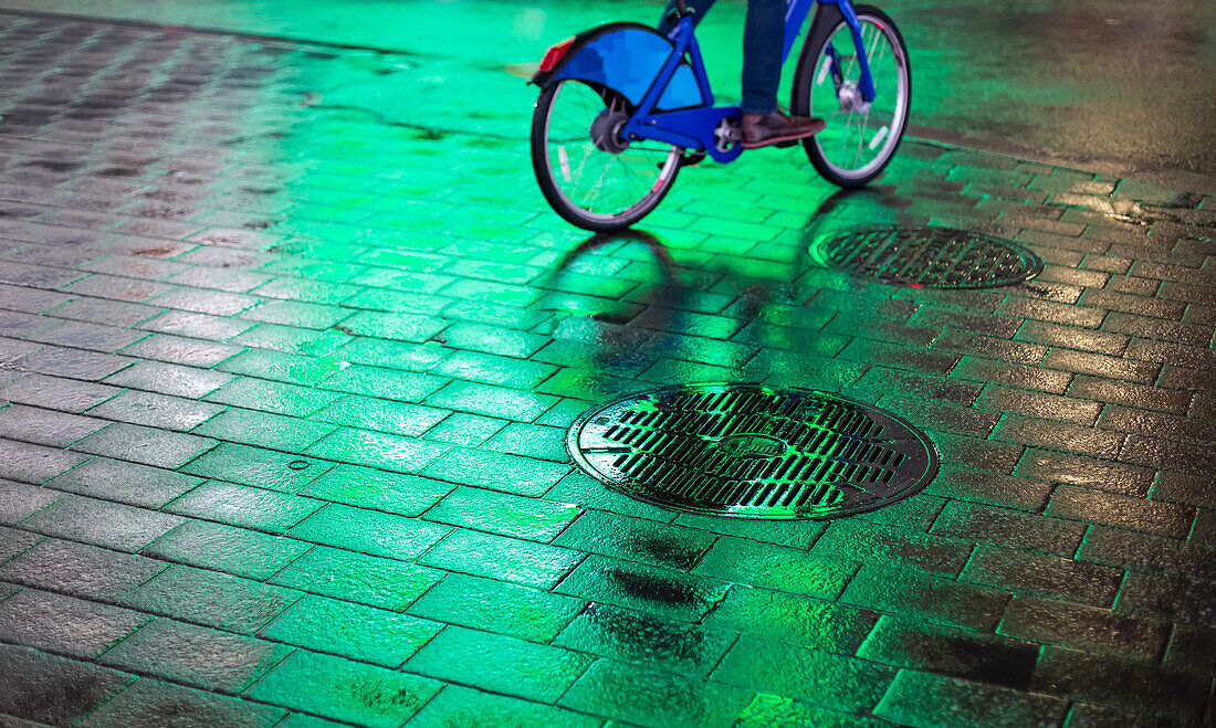 Radfahrer auf nassem Gehweg mit leuchtendem grünen Licht bei Nacht in Manhattan; New York City, New York, Vereinigte Staaten von Amerika