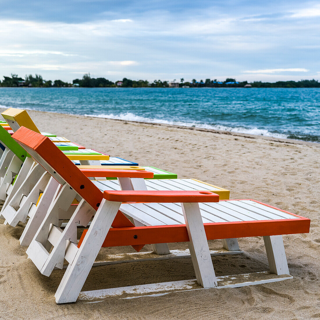 Bunte Liegestühle am Strand in einer Reihe auf dem Sand am Wasser, Placencia Peninsula; Placencia, Belize