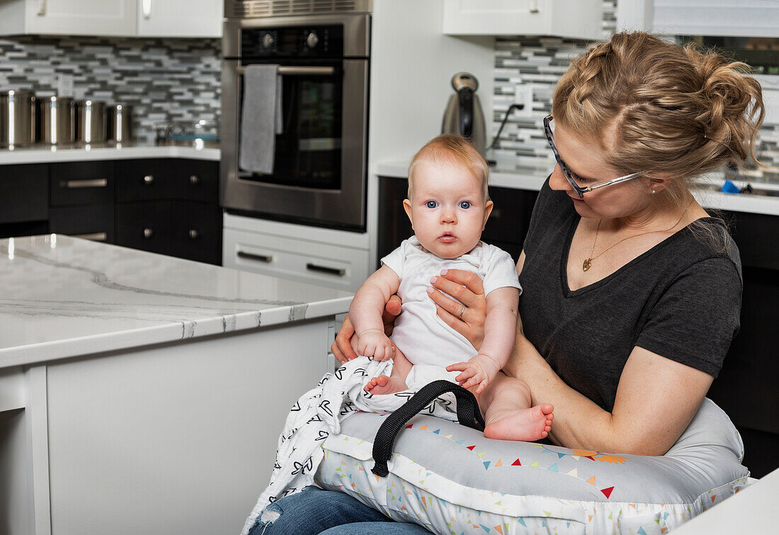 Eine querschnittsgelähmte Mutter hält ihr Baby auf dem Schoß in ihrer Küche, während sie im Rollstuhl sitzt: Edmonton, Alberta, Kanada