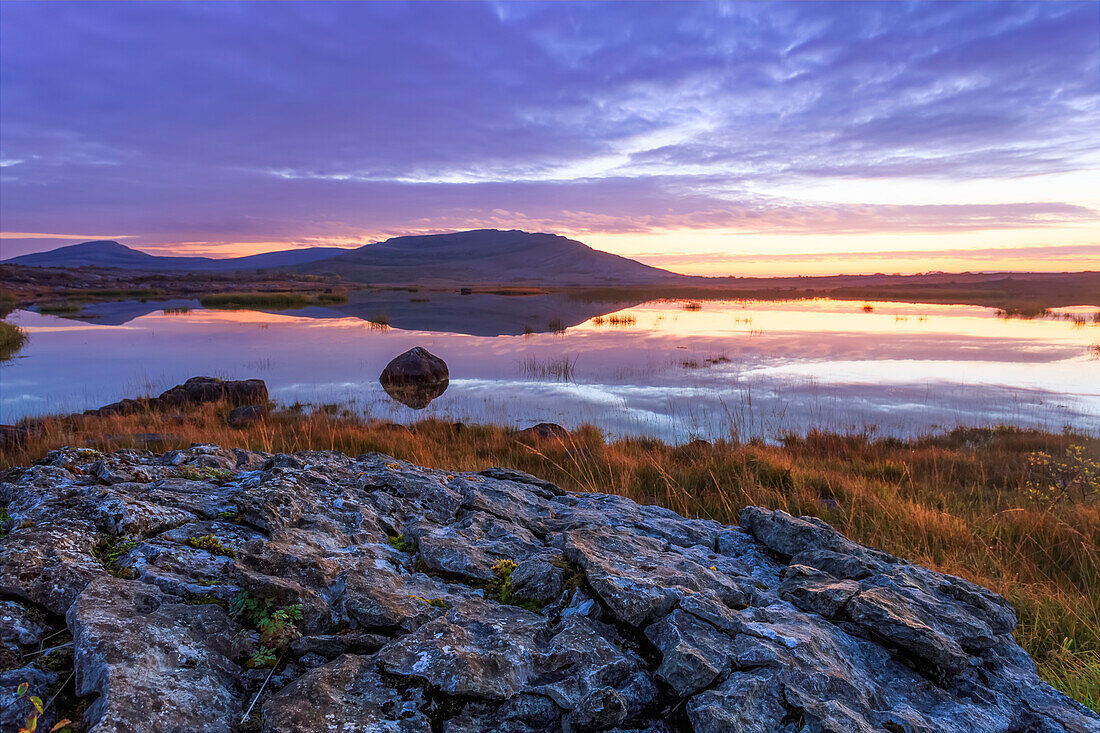 Small lake in the Burren National Park with a small hill in the background at dawn, Burren National Park; County Clare, Ireland