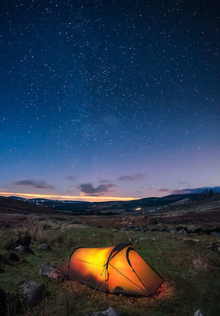 A lit up tent pitched in the Wicklow Mountains at night with stars in the sky; County Wicklow, Ireland