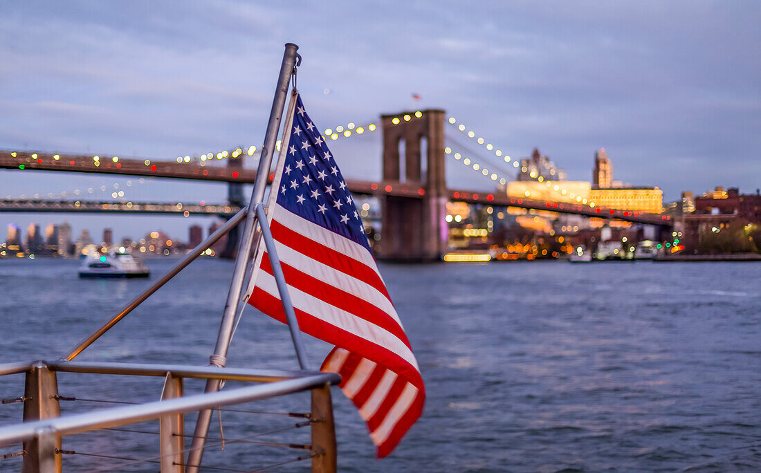 An American Flag flies from a railing at the waterfront with a view of the Brooklyn Bridge, Manhattan; New York City, New York, United States of America