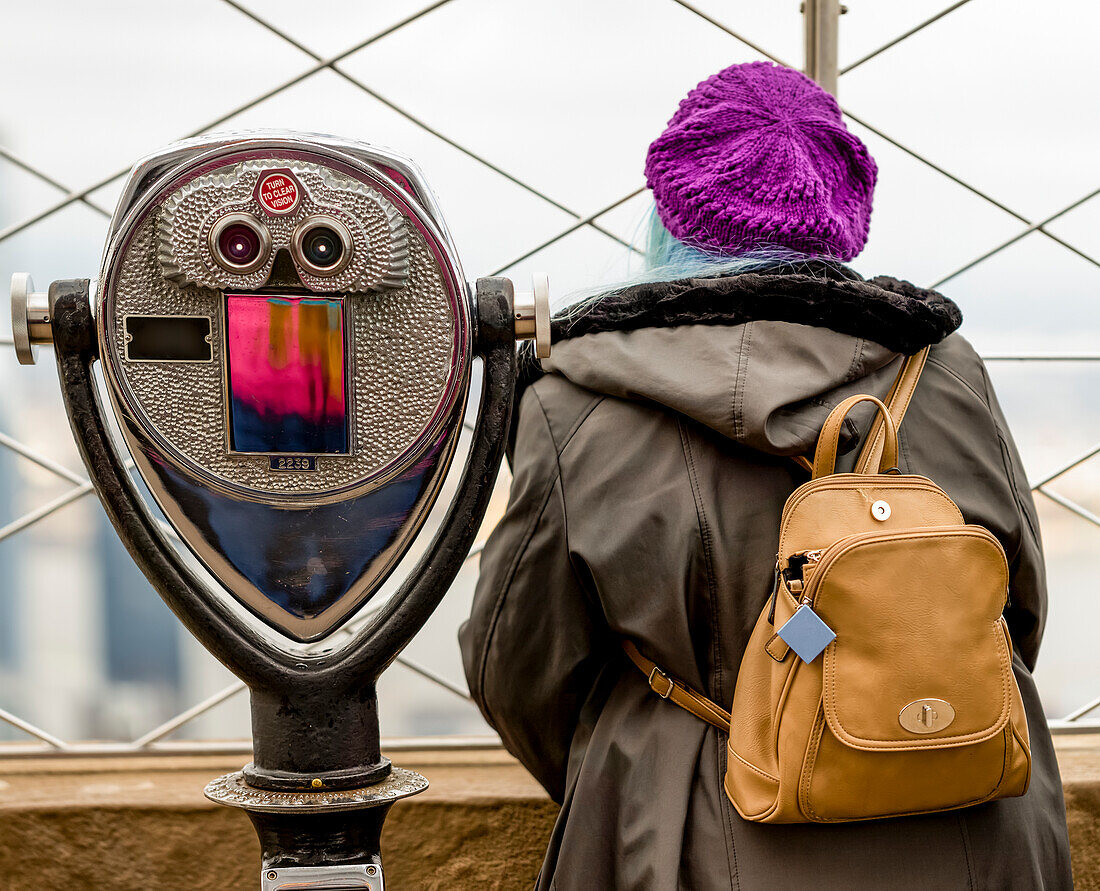 Female tourist standing beside binoculars outside on the observation deck at the Empire State Building in Midtown Manhattan; New York City, New York, United States of America