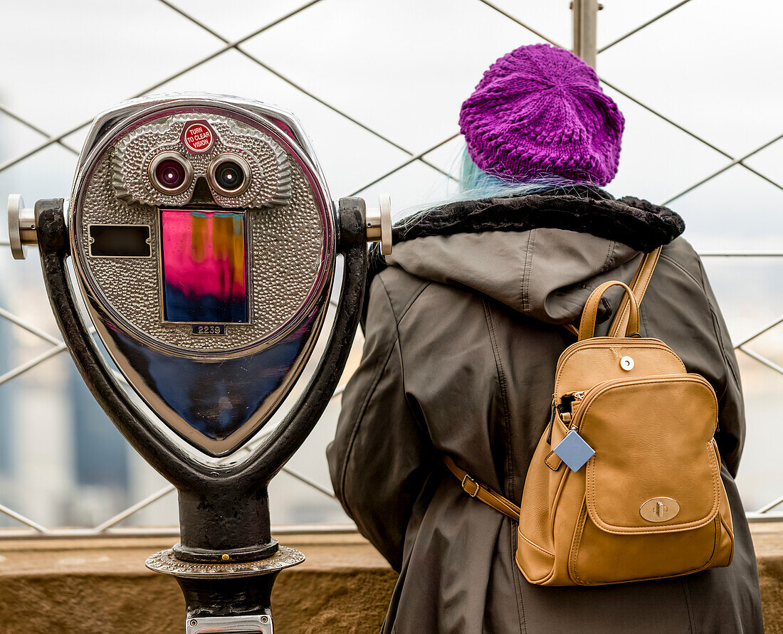 Weibliche Touristin steht neben einem Fernglas auf der Aussichtsplattform des Empire State Building in Midtown Manhattan; New York City, New York, Vereinigte Staaten von Amerika