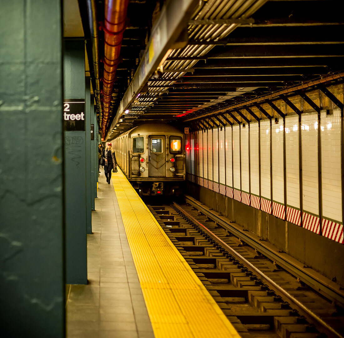 Underground subway on tracks with people walking on platform; New York City, New York, United States of America