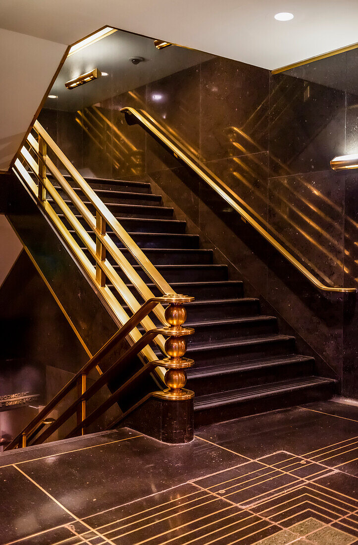 Staircase with brass handrails inside a building with dark brown flooring and walls; New York City, New York, United States of America