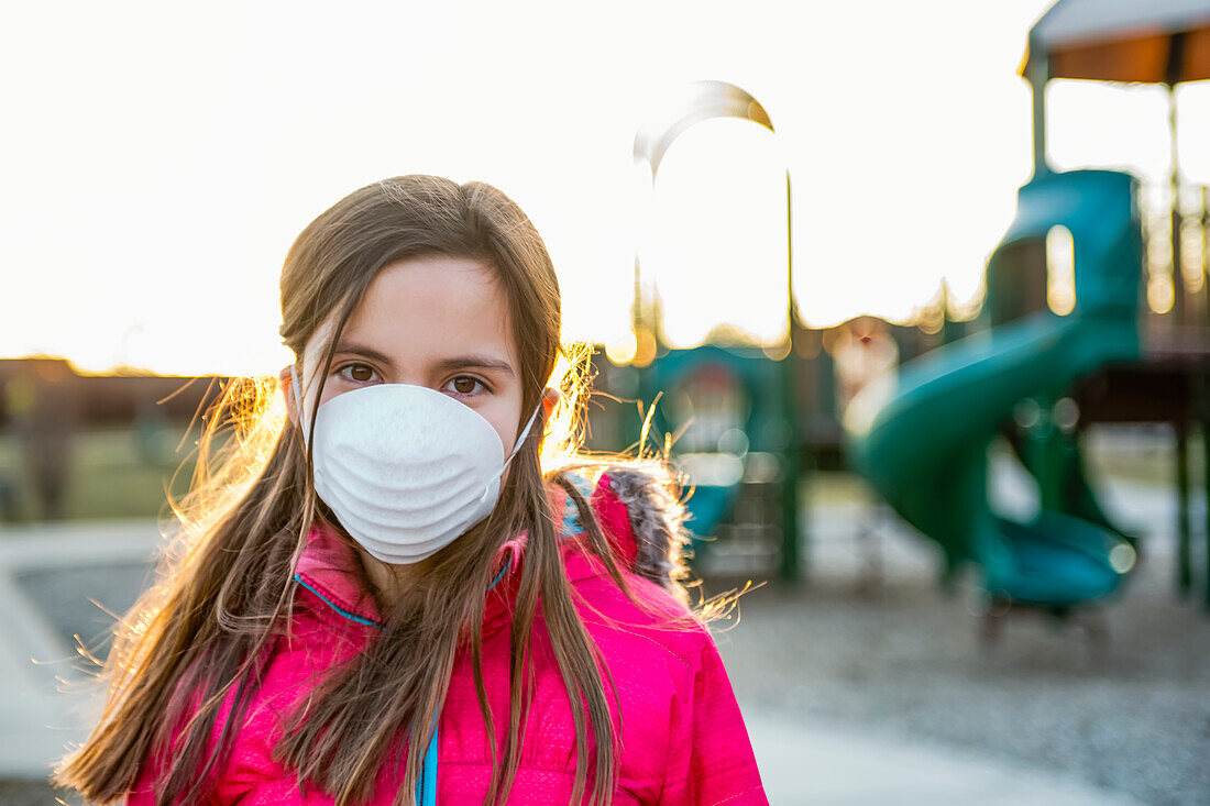 Junges Mädchen steht auf einem Spielplatz und trägt eine Schutzmaske zum Schutz gegen COVID-19 während der weltweiten Coronavirus-Pandemie; Toronto, Ontario, Kanada