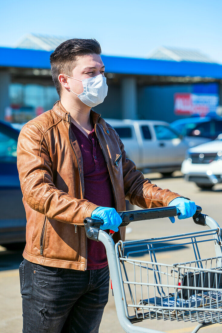 Ein junger Mann steht während der Covid-19-Weltpandemie mit einem Einkaufswagen auf einem Parkplatz an; Edmonton, Alberta, Kanada