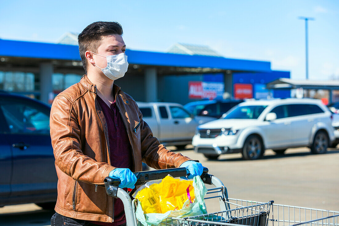 Ein junger Mann steht mit einem Einkaufswagen auf einem Parkplatz während der Covid-19-Weltpandemie; Edmonton, Alberta, Kanada