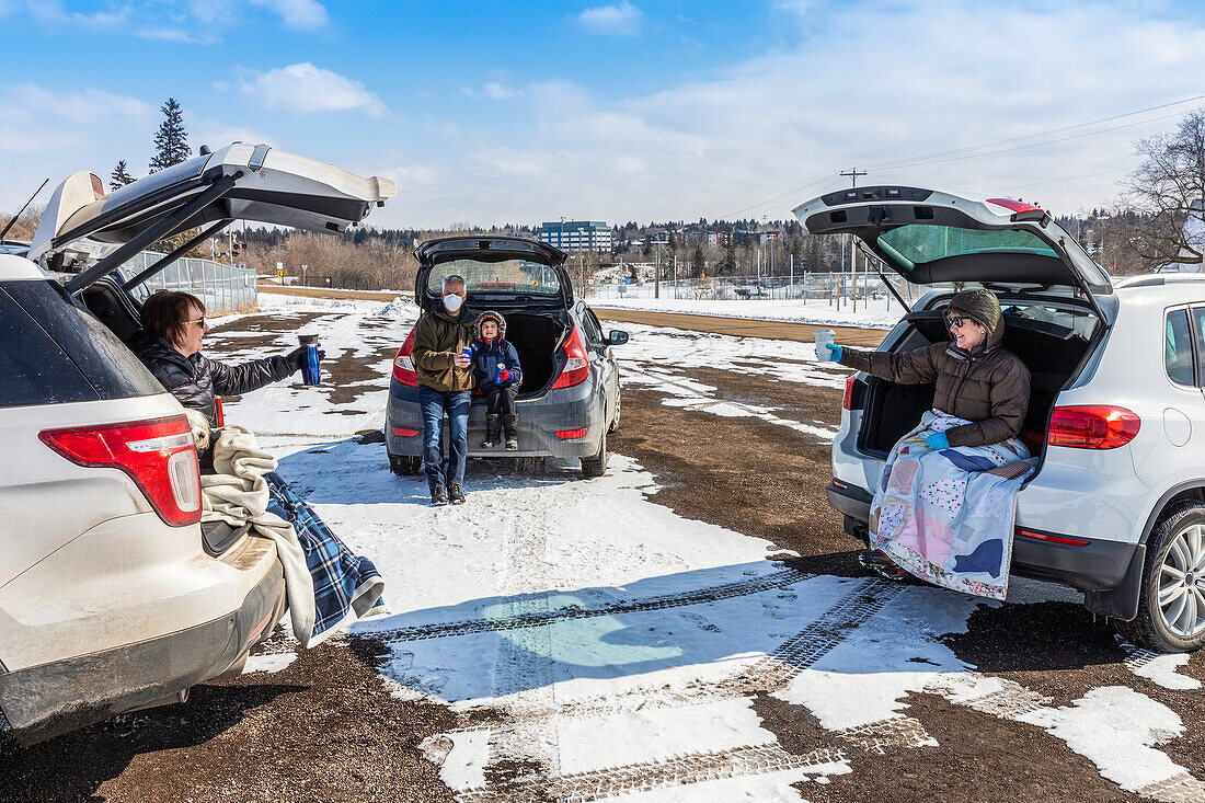 Families sit in the back of their vehicles in a parking lot to visit during the Covid-19 world pandemic; St. Albert, Alberta, Canada