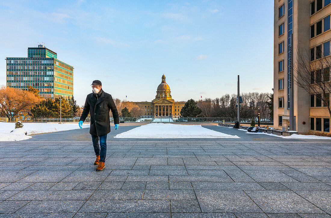 Ein Mann mit Maske und Handschuhen geht während der Covid-19-Weltpandemie auf einem Weg neben der Legislative; Edmonton, Alberta, Kanada