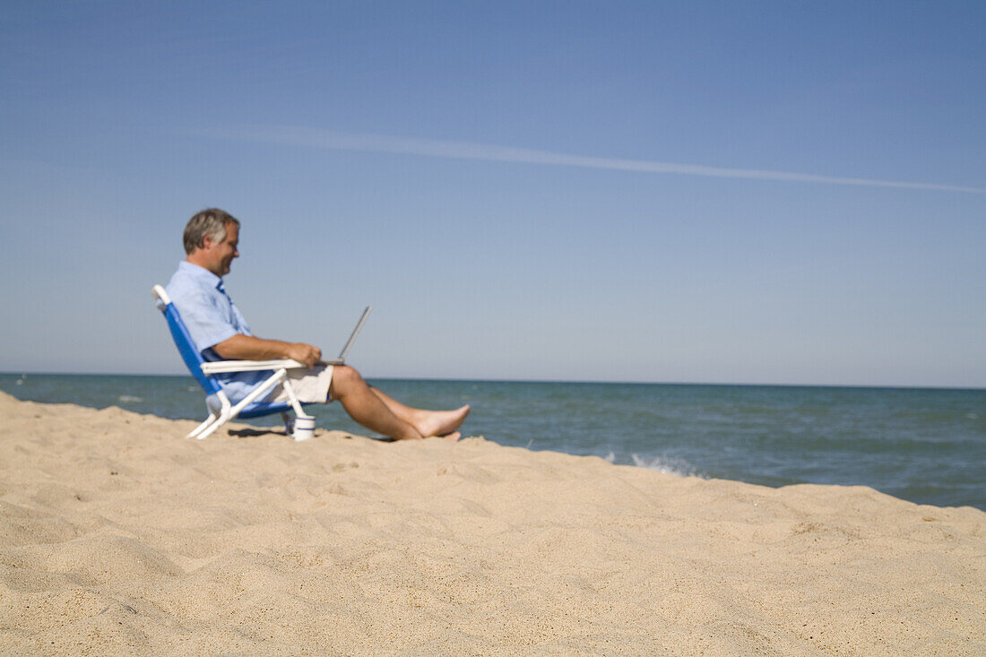 Mann sitzt am Strand und benutzt einen Laptop, Lake Michigan, USA