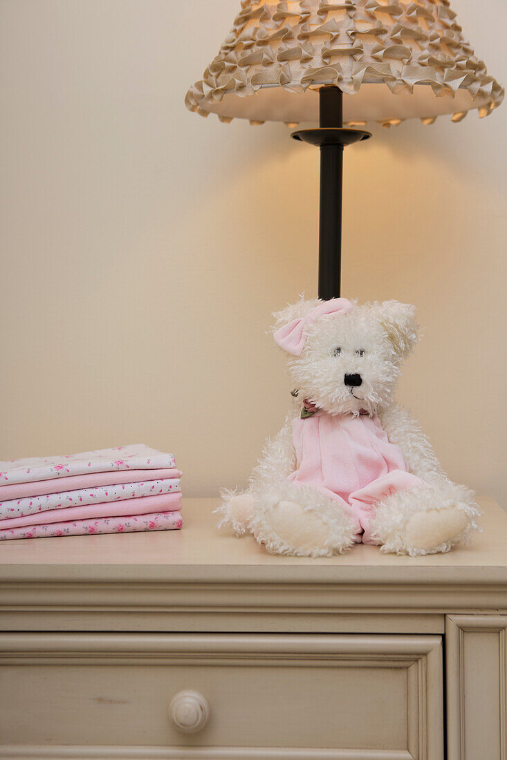 Stack of Baby Blankets on Dresser next to Teddy Bear and Lamp in Nursery