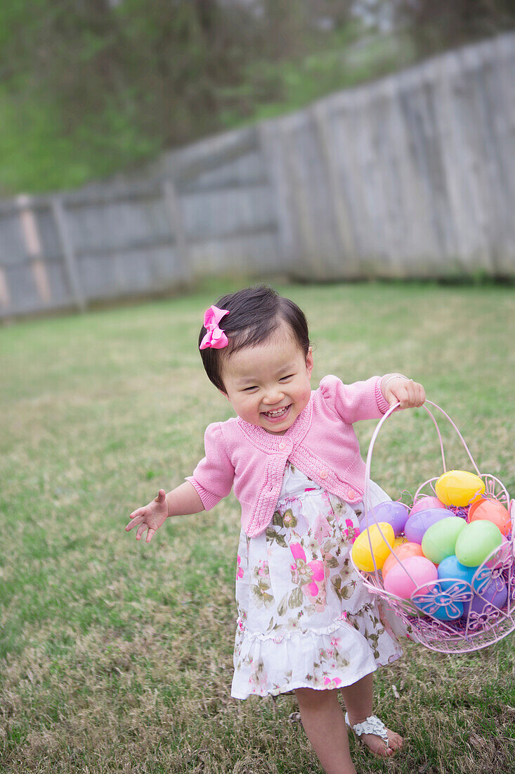 Kleinkind-Mädchen rennt und lächelt mit vollem Ostereier-Körbchen