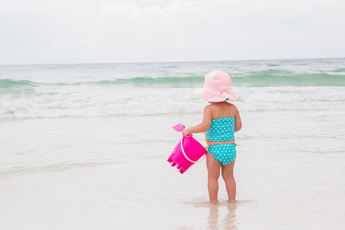 Kleines Mädchen spielt mit Schaufel und Eimer im Meer am Strand, Destin, Florida, USA