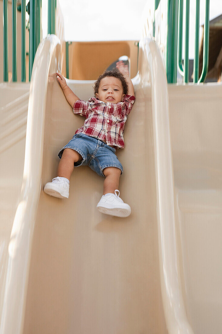 Junger Junge rutscht auf dem Spielplatz die Rutsche hinunter