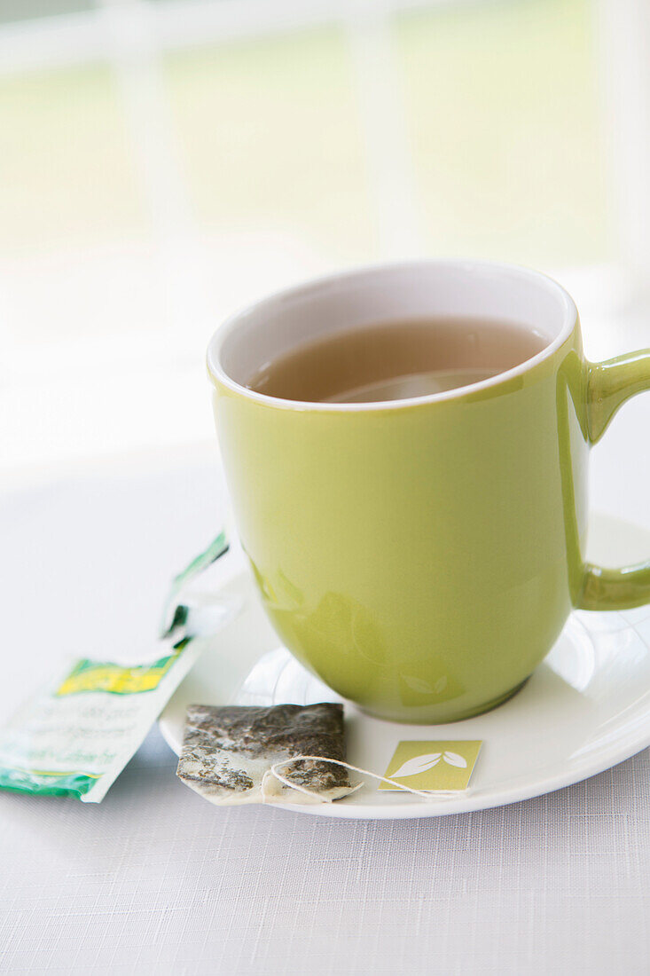 Benutzter Teebeutel auf Untertasse mit Tasse Tee in grüner Tasse, Studioaufnahme