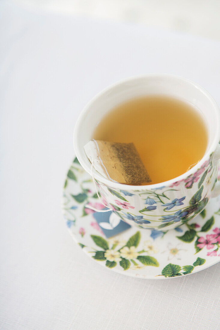 Teetasse in hübscher Blumentasse mit Untertasse auf weißem Hintergrund, Studioaufnahme