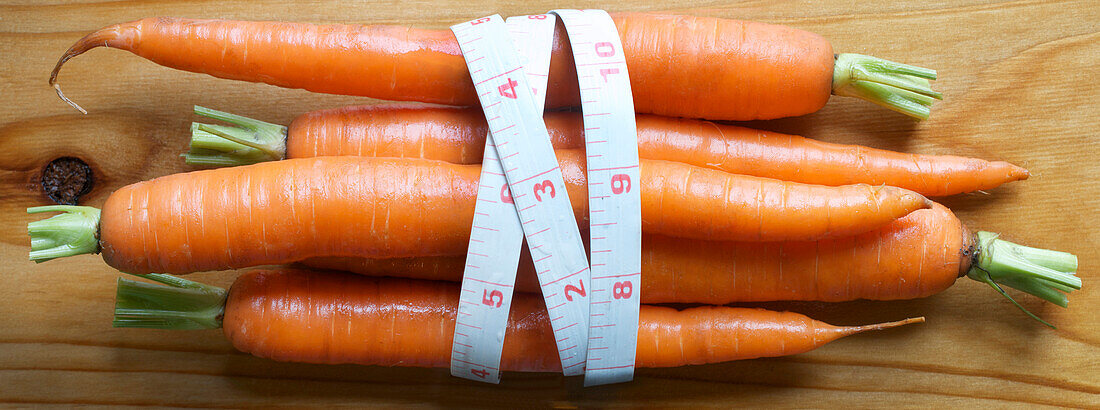 view of fresh carrots on cedar board with measuring tape wrap