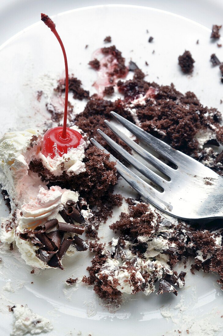 Nahaufnahme von halb gegessener Schwarzwälder Kirschtorte auf weißem Teller mit Gabel, Studioaufnahme