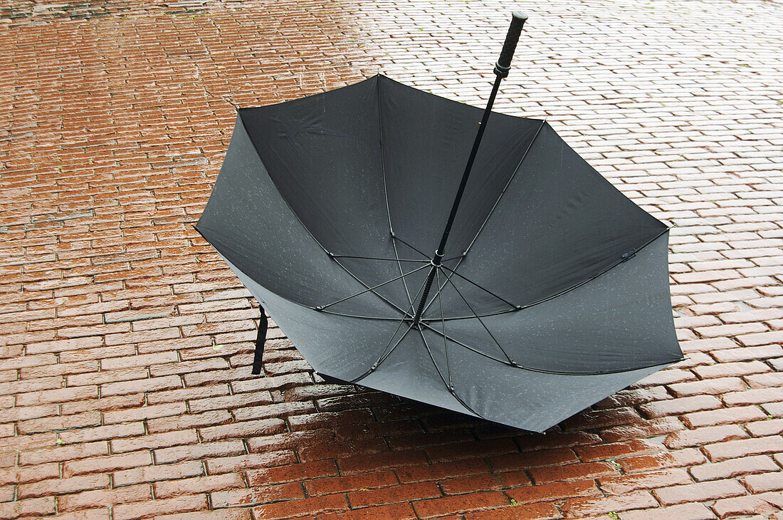 Geöffneter Regenschirm auf nassem Kopfsteinpflaster liegend