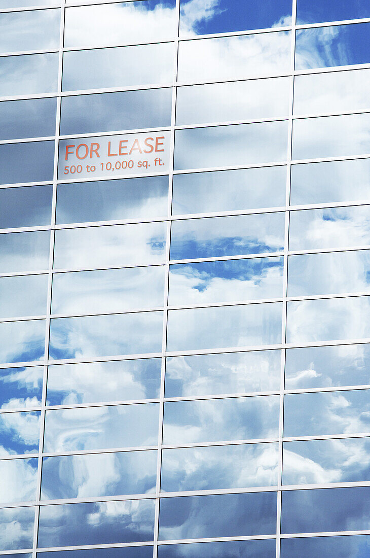 Himmel und Wolken spiegeln sich in Gebäudefenstern mit einem Schild "Zu vermieten