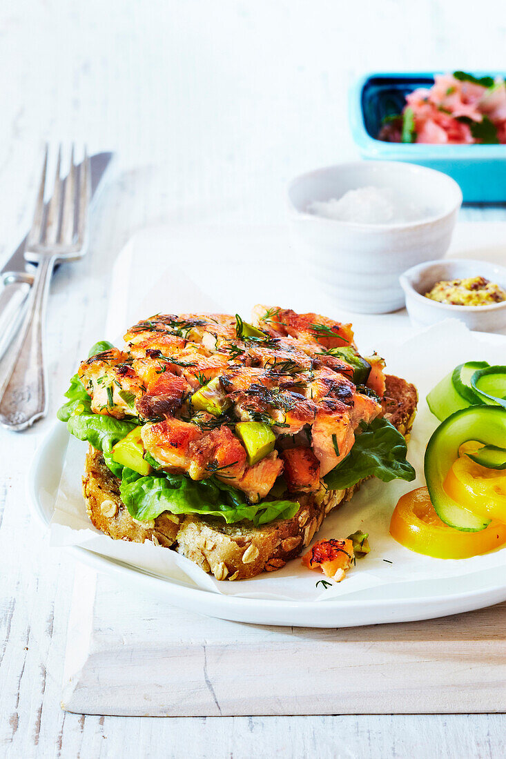 Salmon and avocado burger on whole grain bread on plate, studio shot