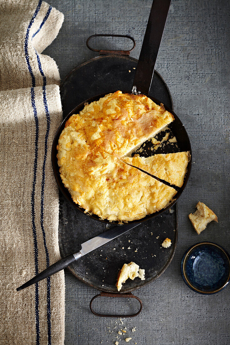 Cheesy Bannock bread in baking pan on grey background, studio shot