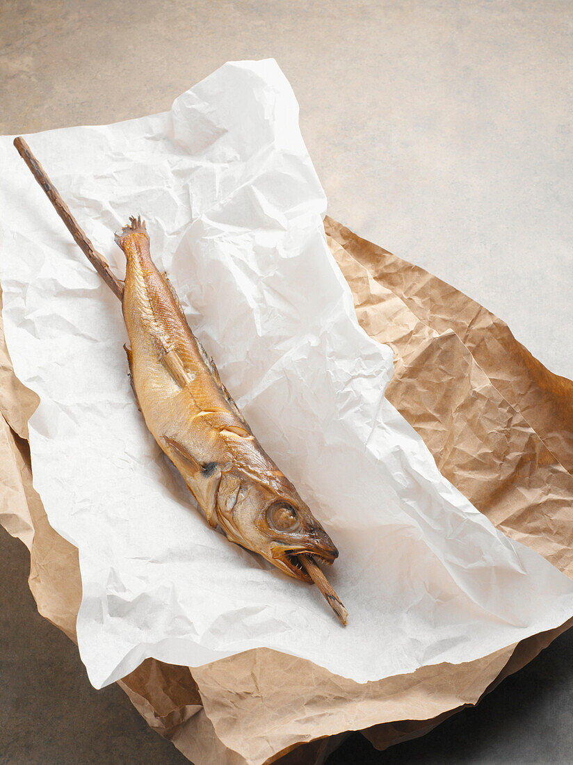 Fried mackerel pike fish on stick, in paper wrapper, studio shot