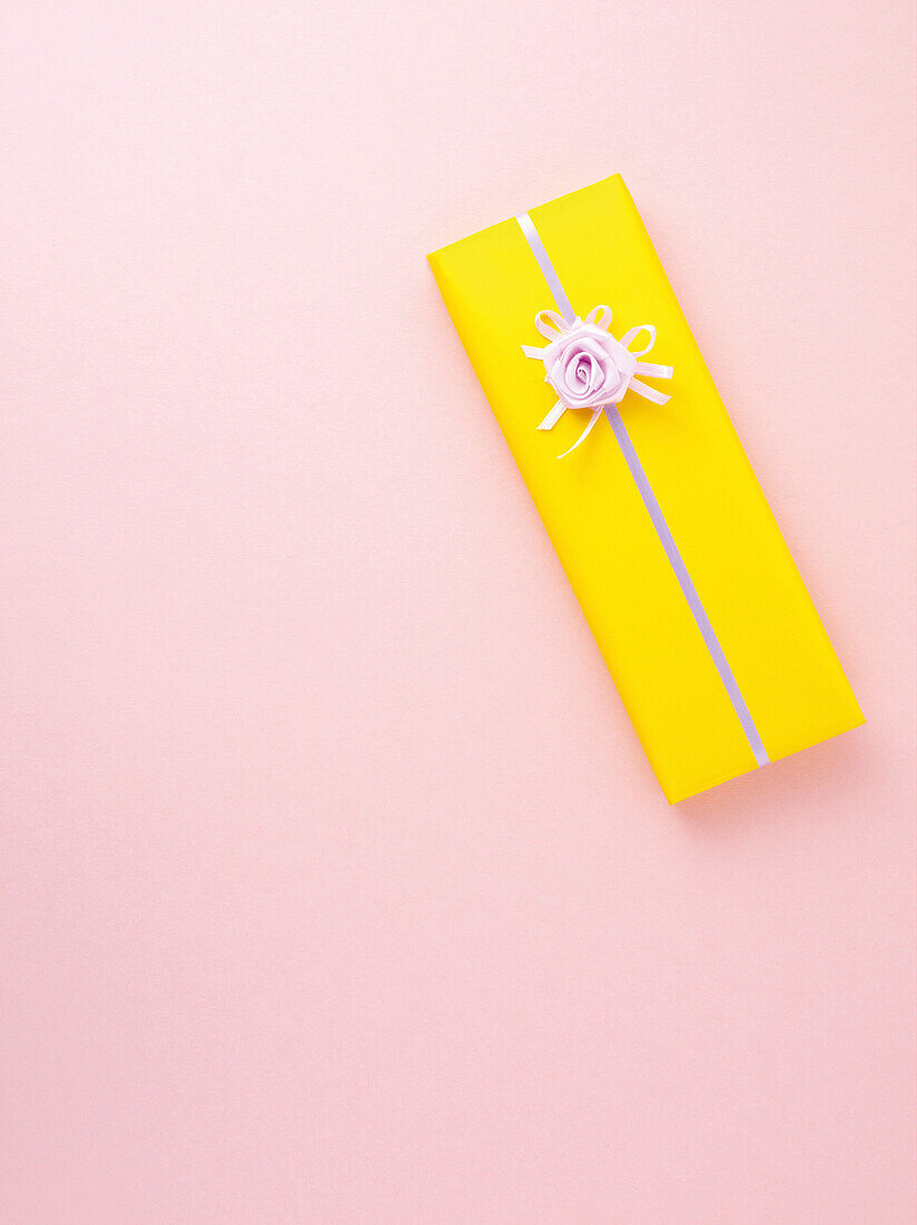 In gelbes Geschenkpapier eingewickeltes Geschenk auf rosa Hintergrund, Studioaufnahme