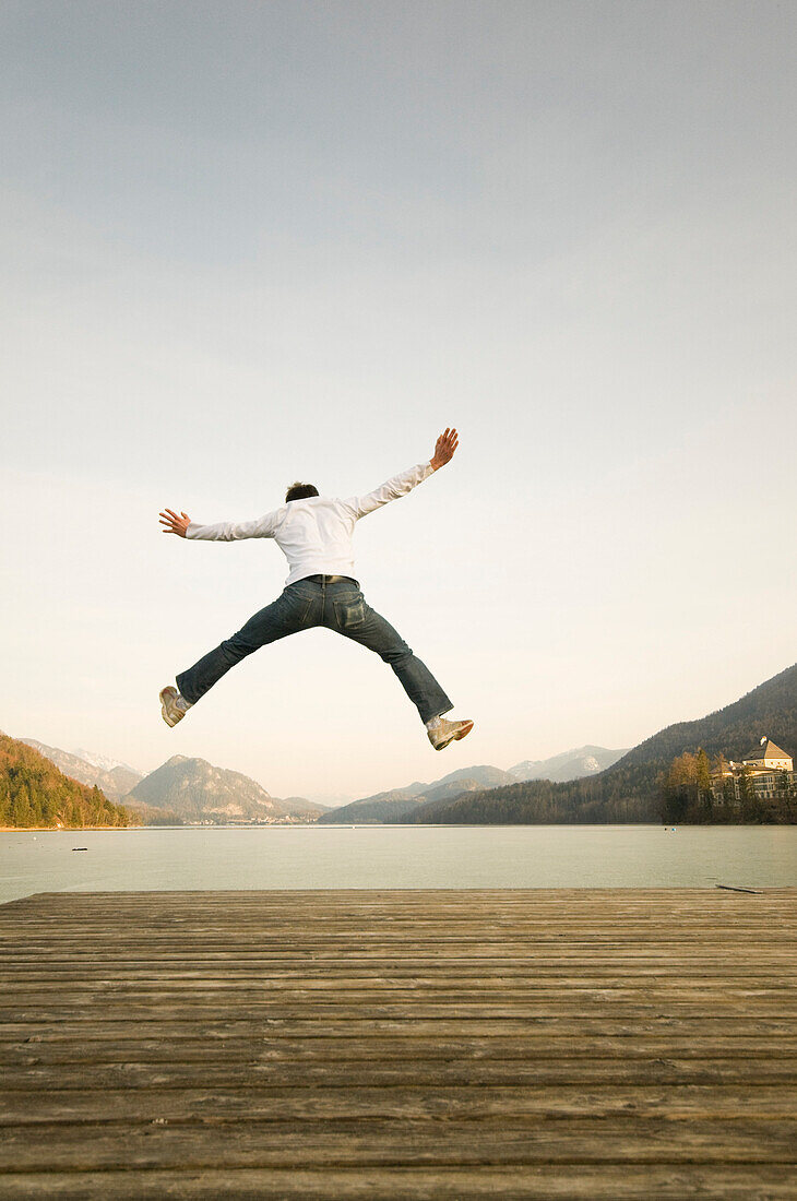 Mann auf dem Steg springt hoch in die Luft, Fuschlsee, Salzburger Land, Österreich