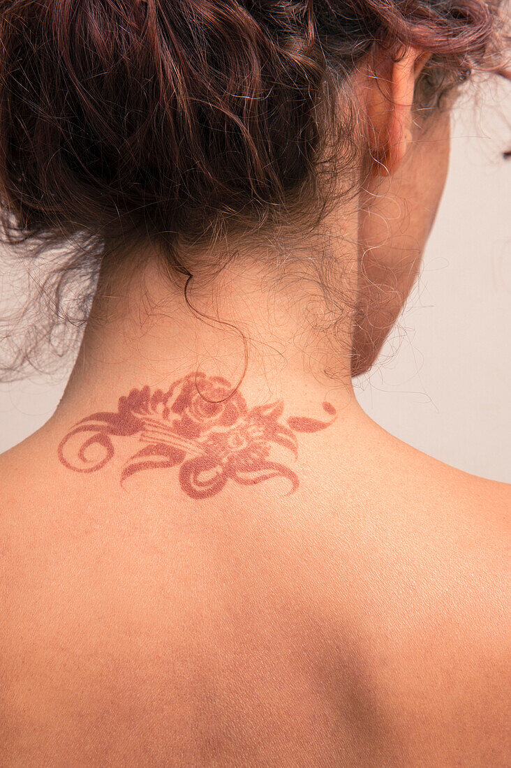 Close-up of woman's back and neck showing detail of henna painted tattoo in arabic style, studio shot on white background