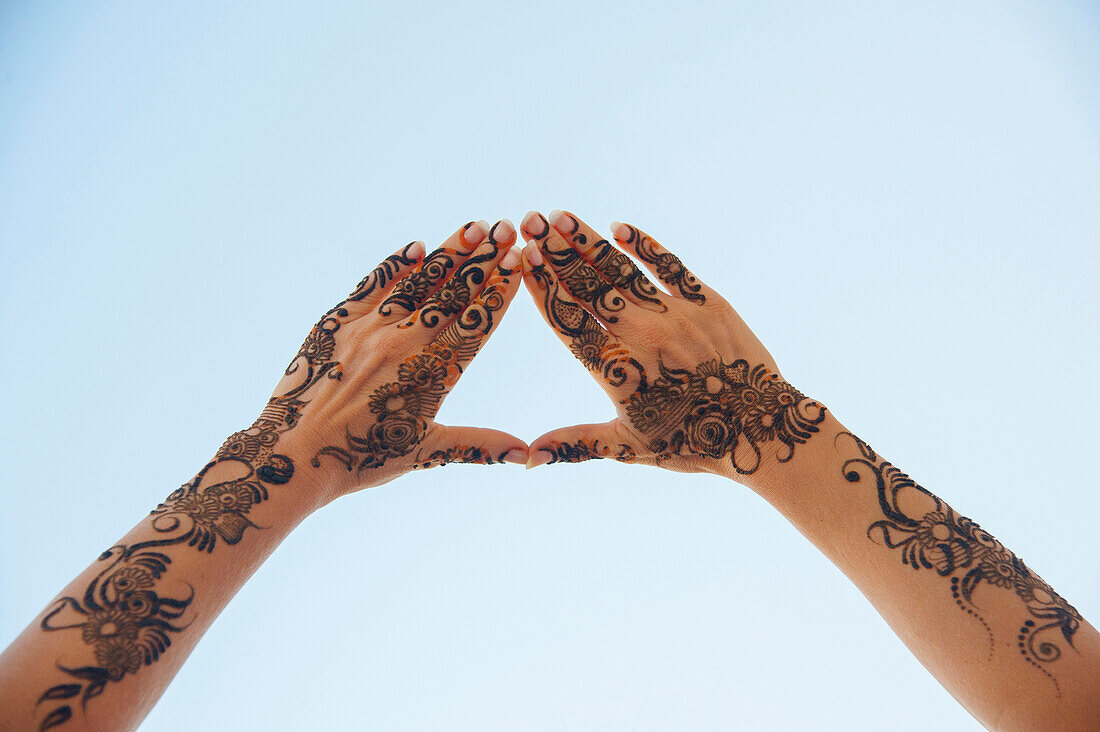 Woman's Hands and Arms Painted with Henna in Arabic Style, forming Triangle with Fingers against Blue Sky, Muscat, Oman