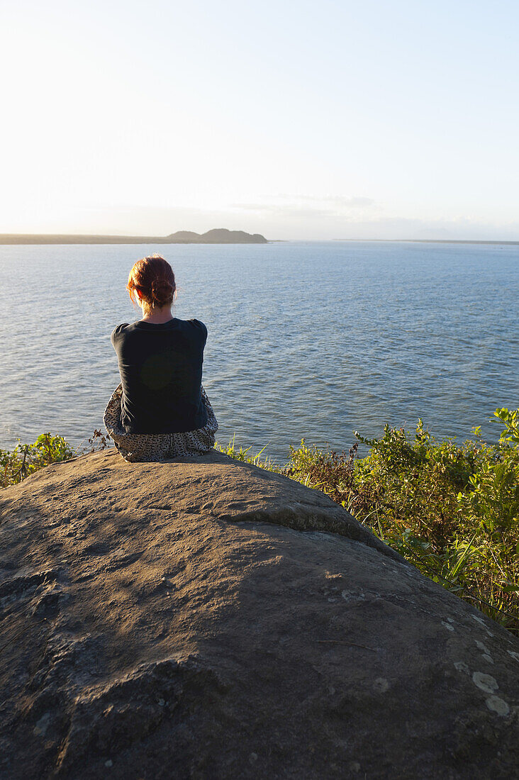 Rückenansicht einer Frau, die auf einem Felsen sitzt, Ilha do Mel, Parana, Brasilien