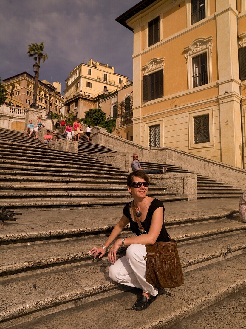 Weibliche Touristin sitzt auf einer Stufe am Spanischen Platz und lächelt; Rom, Italien