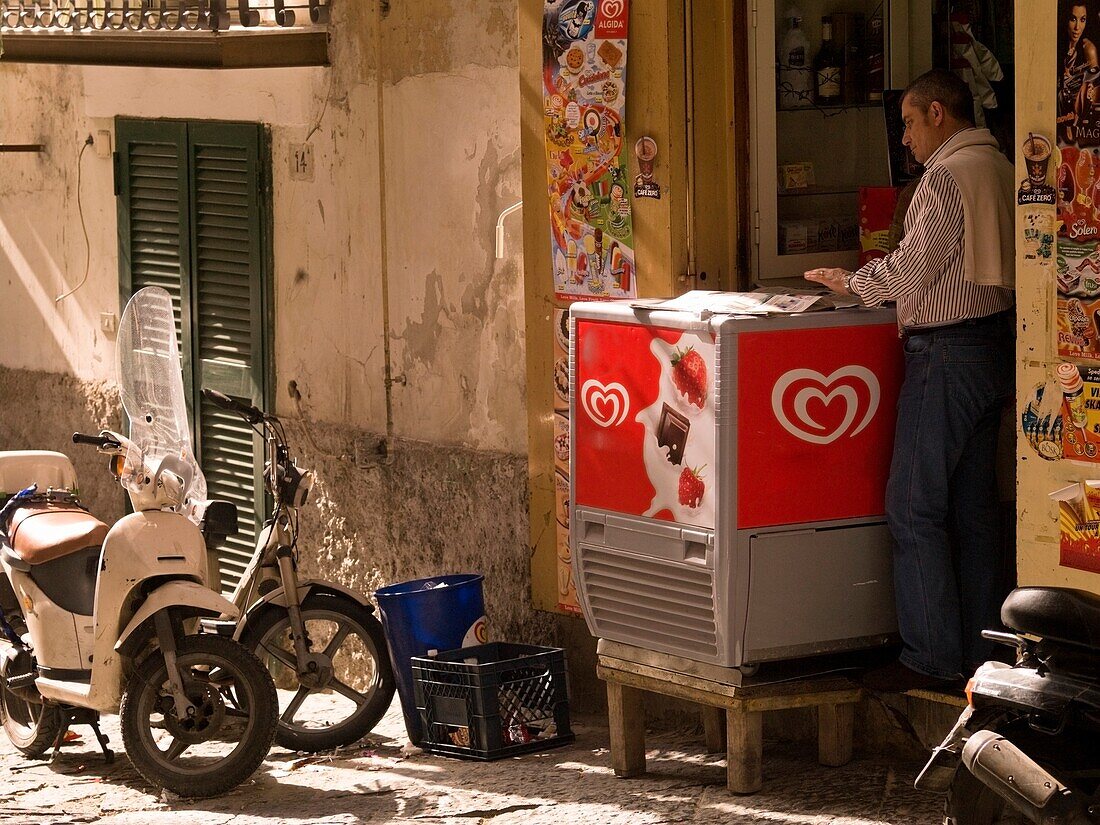 Mann liest Zeitung vor einem kleinen Laden; Neapel, Italien